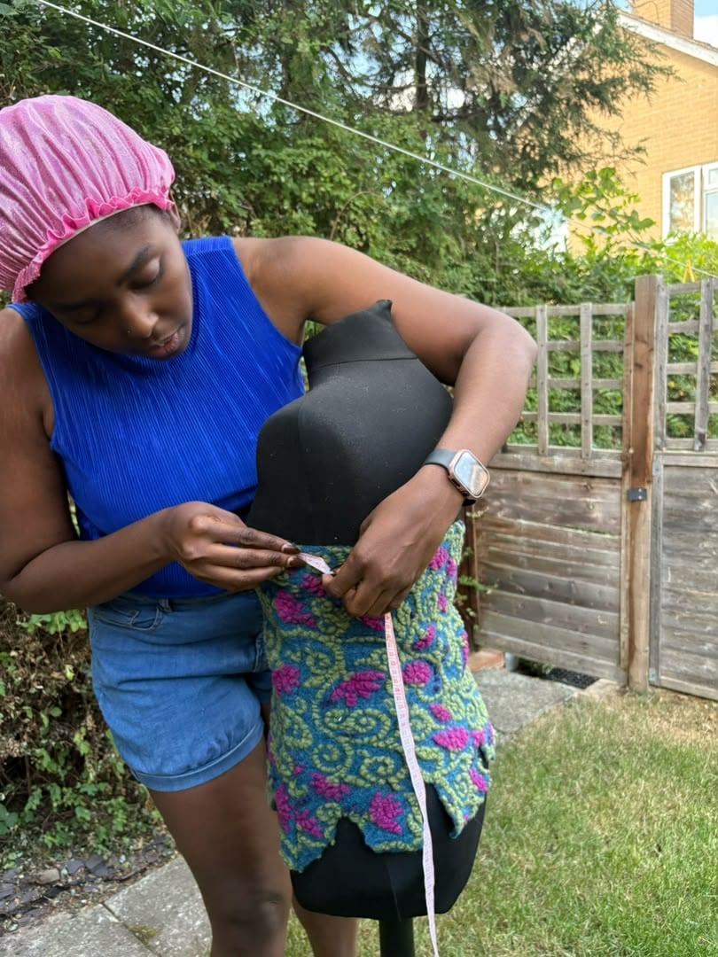 Adora Vanessa Mofunanya measuring a wax-print garment on a dress form in the garden